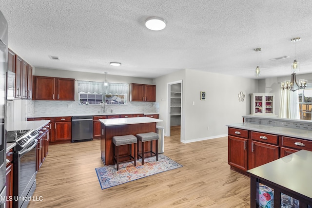 kitchen featuring sink, appliances with stainless steel finishes, a kitchen island, a kitchen bar, and decorative light fixtures