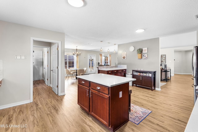 kitchen with stainless steel refrigerator, hanging light fixtures, light hardwood / wood-style floors, a textured ceiling, and a kitchen island