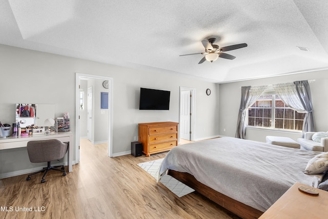 bedroom featuring light wood-type flooring, a textured ceiling, ceiling fan, and a tray ceiling