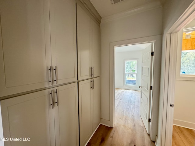 hall with crown molding, light wood finished floors, visible vents, and baseboards