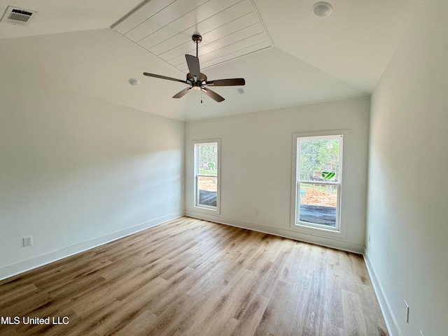 empty room featuring plenty of natural light, visible vents, vaulted ceiling, and wood finished floors