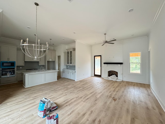 kitchen featuring stainless steel oven, ceiling fan with notable chandelier, light hardwood / wood-style flooring, an island with sink, and black microwave