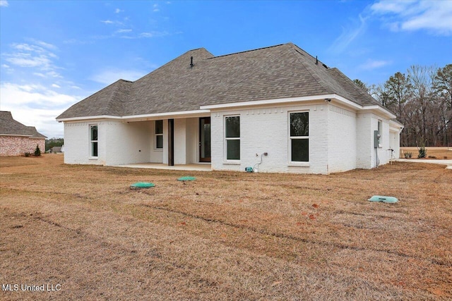 back of house featuring a shingled roof, a patio area, a lawn, and brick siding