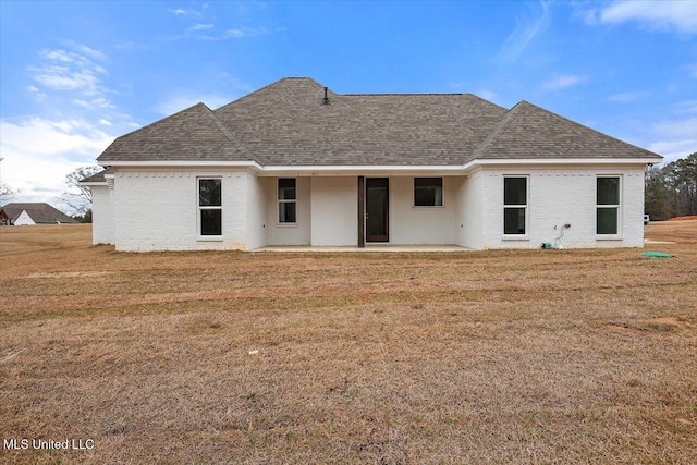 rear view of house with roof with shingles, a patio, and a lawn