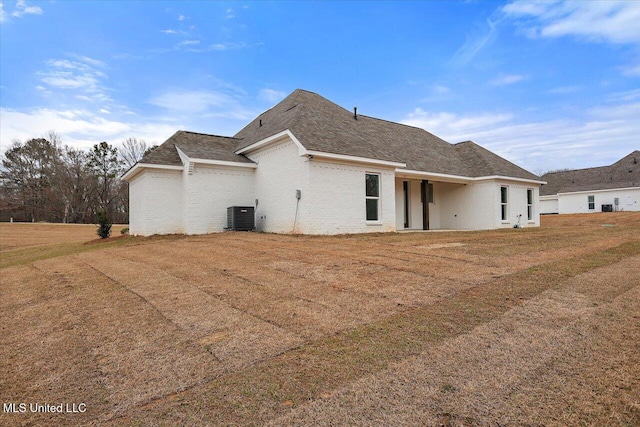 back of house featuring a lawn, central AC, and roof with shingles