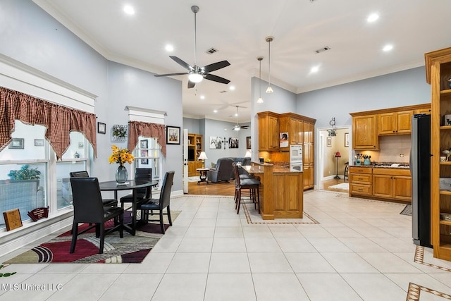 kitchen with ceiling fan, a towering ceiling, a breakfast bar area, light tile patterned floors, and ornamental molding