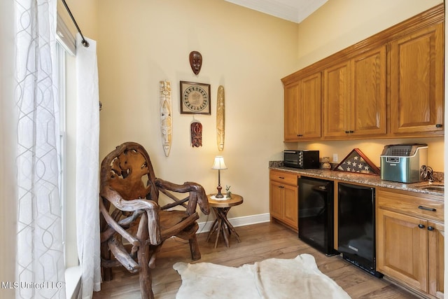 bar with light wood-type flooring, refrigerator, stone countertops, and ornamental molding