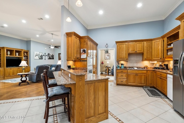 kitchen featuring a breakfast bar, ceiling fan, light stone countertops, light tile patterned floors, and appliances with stainless steel finishes