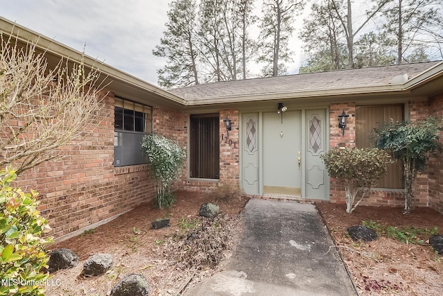 property entrance featuring brick siding and roof with shingles