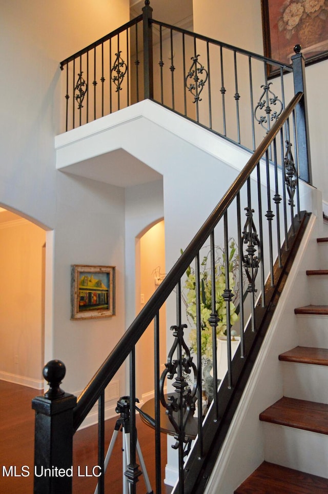 stairway featuring a towering ceiling and wood-type flooring