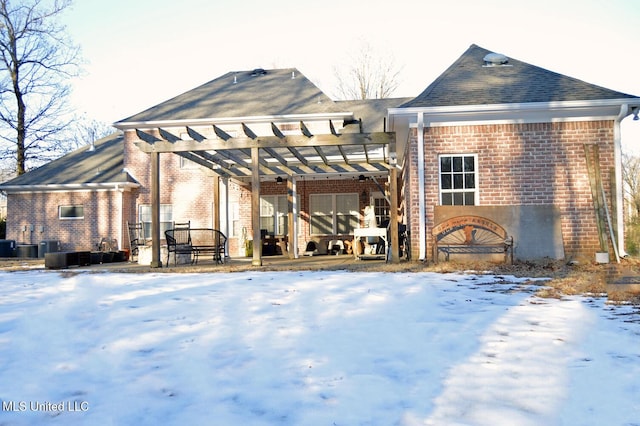 snow covered back of property with a pergola