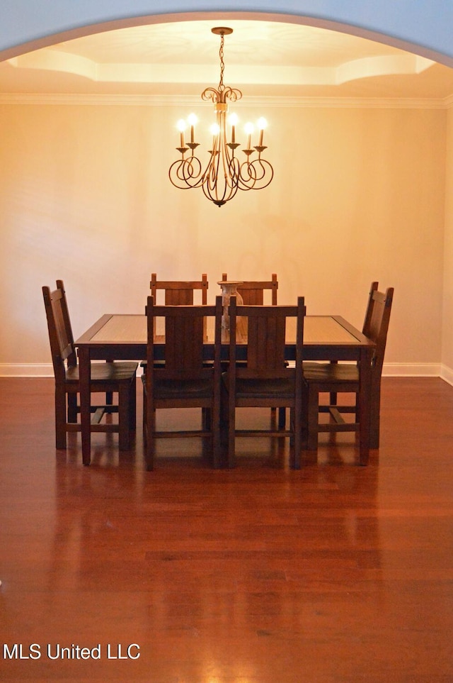 dining area with a raised ceiling, a chandelier, and dark wood-type flooring