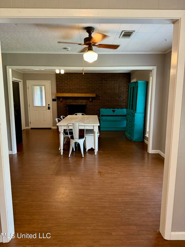 unfurnished dining area with ceiling fan, dark hardwood / wood-style flooring, ornamental molding, a fireplace, and brick wall