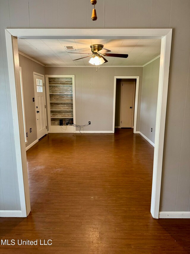 unfurnished room featuring dark wood-type flooring, ceiling fan, crown molding, and a fireplace