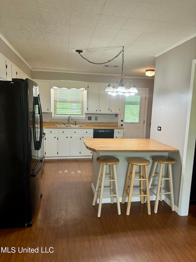 kitchen with white cabinets, hanging light fixtures, a kitchen bar, black appliances, and sink