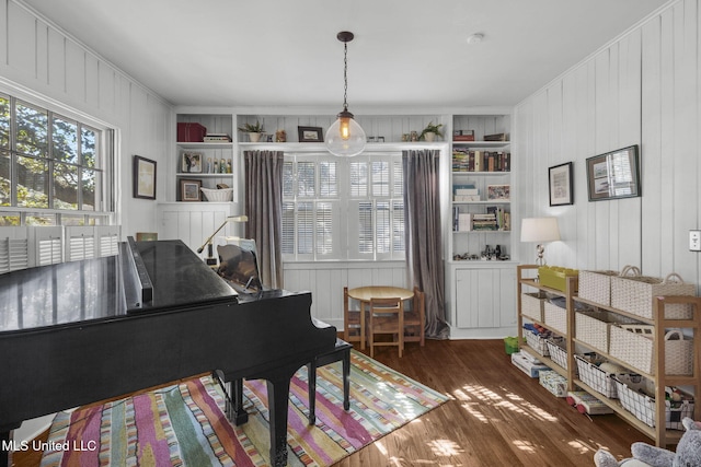 sitting room with built in shelves, dark wood-type flooring, ornamental molding, and wood walls