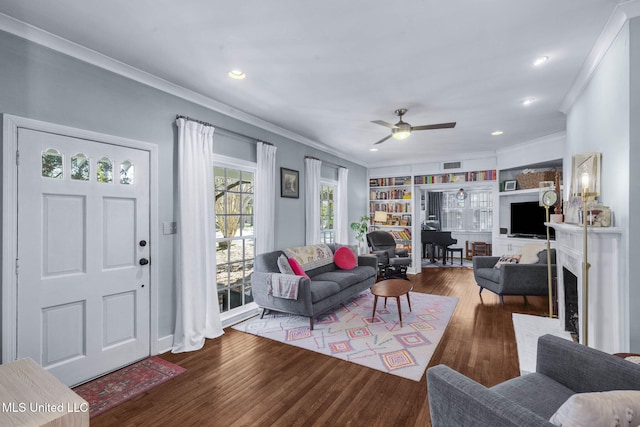 living room featuring built in shelves, ceiling fan, ornamental molding, and hardwood / wood-style flooring