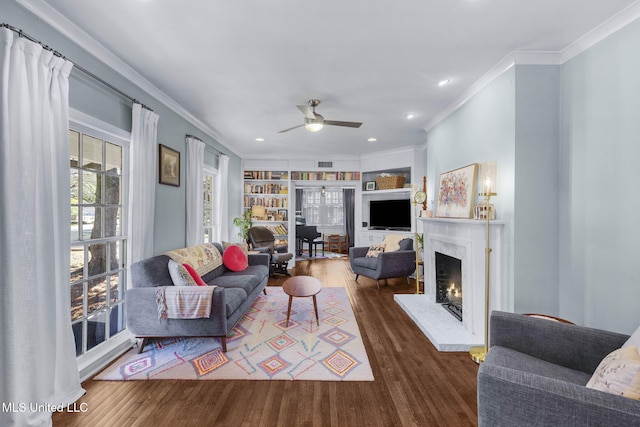 living room featuring wood-type flooring, ceiling fan, built in features, and a fireplace