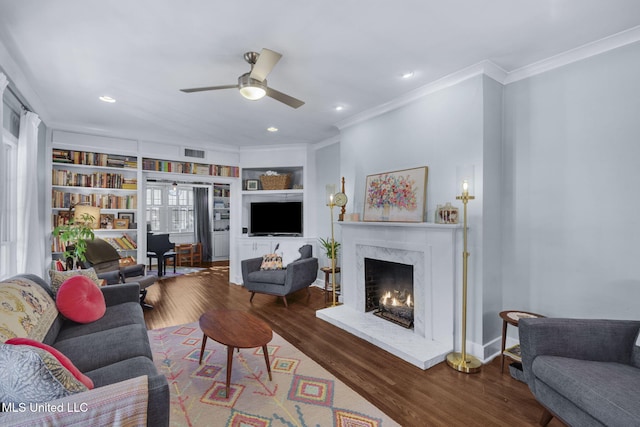 living room featuring built in shelves, ornamental molding, hardwood / wood-style flooring, ceiling fan, and a fireplace