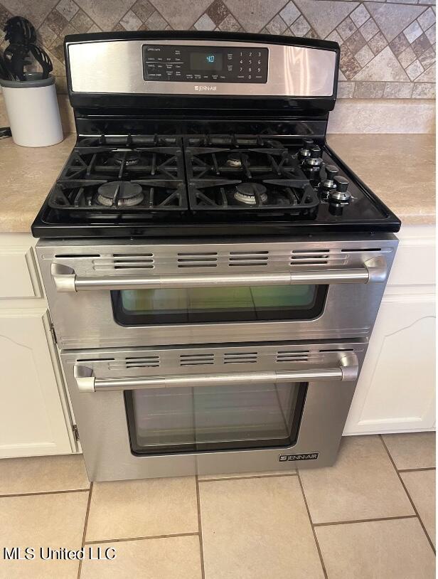 interior details featuring white cabinets, double oven range, and light tile patterned floors