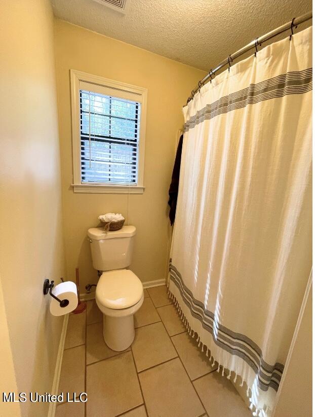 bathroom with walk in shower, toilet, tile patterned floors, and a textured ceiling