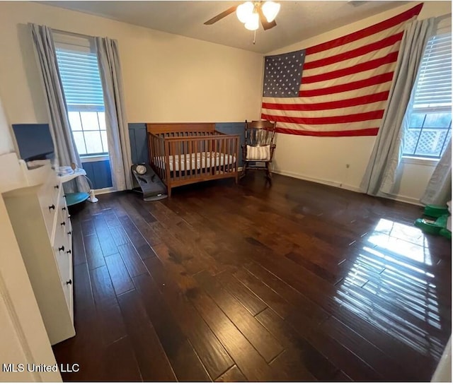 bedroom featuring ceiling fan, dark hardwood / wood-style floors, and a crib