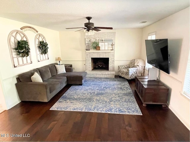 living room with dark wood-type flooring, ceiling fan, and a brick fireplace