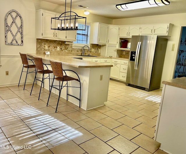 kitchen featuring white cabinets, hanging light fixtures, a kitchen bar, stainless steel refrigerator with ice dispenser, and sink