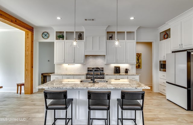 kitchen with decorative light fixtures, a center island with sink, a sink, and freestanding refrigerator