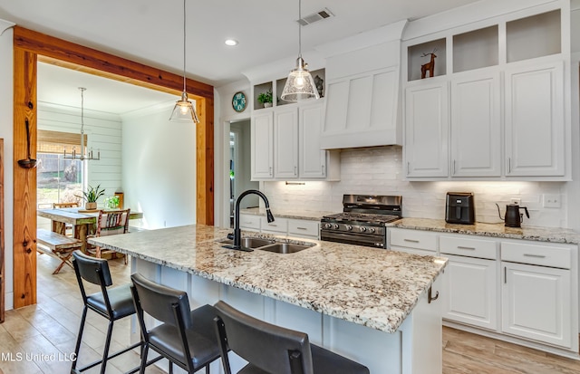 kitchen with an island with sink, decorative light fixtures, a sink, and gas stove