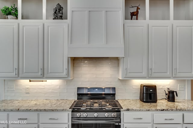 kitchen featuring light stone counters, decorative backsplash, stainless steel gas stove, white cabinetry, and wall chimney range hood