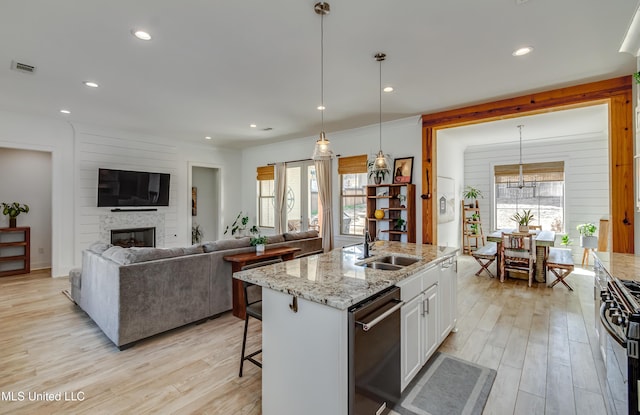 kitchen featuring hanging light fixtures, stainless steel gas stove, white cabinetry, a sink, and an island with sink