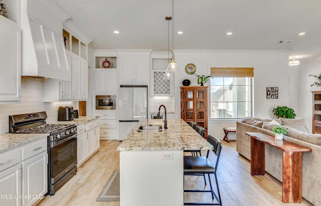 kitchen featuring pendant lighting, custom exhaust hood, stainless steel appliances, open floor plan, and an island with sink