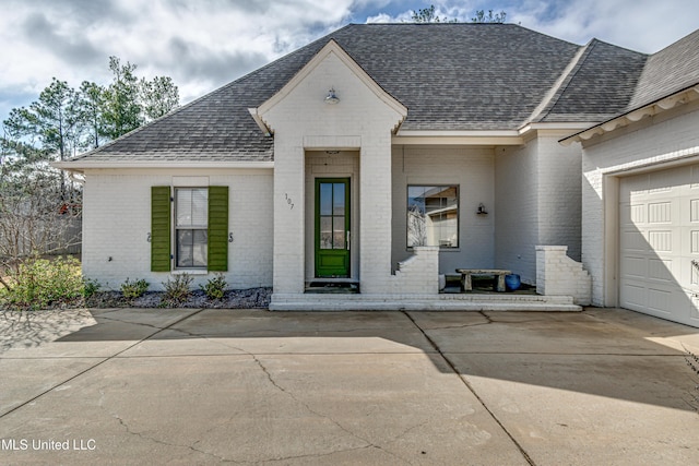 entrance to property with an attached garage, a shingled roof, and brick siding