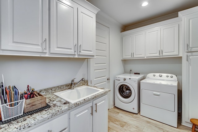 washroom with light wood finished floors, recessed lighting, cabinet space, washing machine and dryer, and a sink