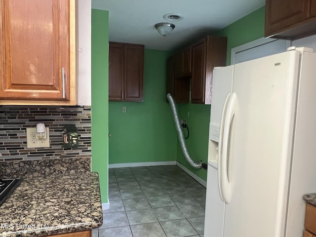 2285 Harkness Ct, Biloxi, MS 39532 - kitchen featuring white fridge with ice dispenser, backsplash, light tile patterned floors, baseboards, and dark stone countertops