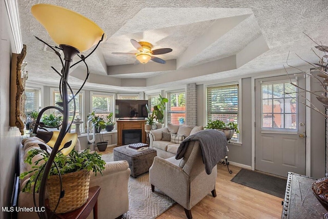 living room featuring a textured ceiling, a tray ceiling, light wood-type flooring, and ceiling fan