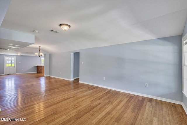 unfurnished living room featuring vaulted ceiling, an inviting chandelier, and light hardwood / wood-style floors