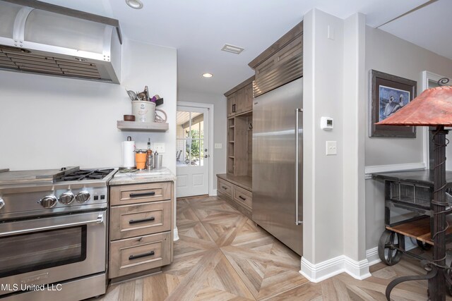 kitchen featuring wall chimney range hood, visible vents, light stone countertops, baseboards, and premium appliances