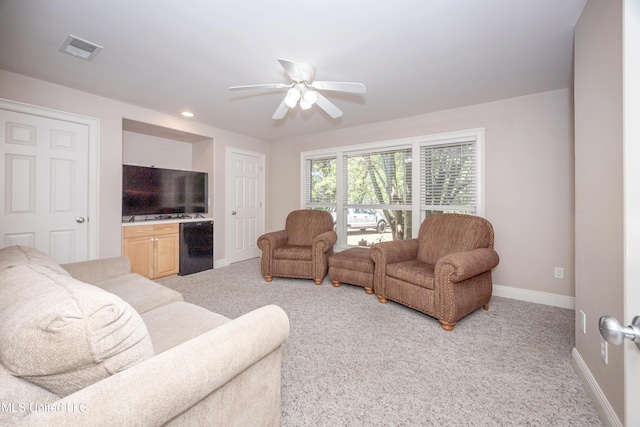 living room featuring light colored carpet, ceiling fan, visible vents, and baseboards