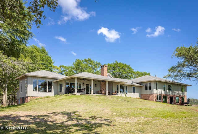 rear view of house featuring a yard, board and batten siding, a ceiling fan, and a chimney