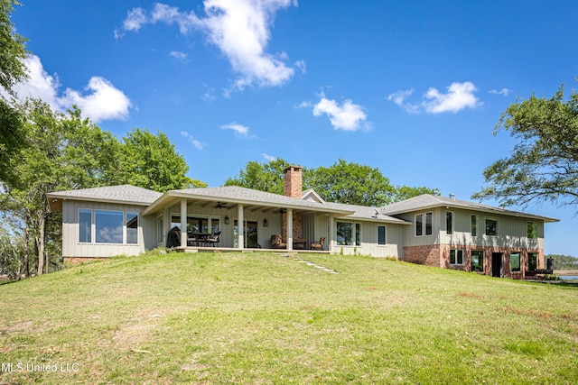 rear view of property featuring board and batten siding, a ceiling fan, a chimney, a lawn, and a shingled roof