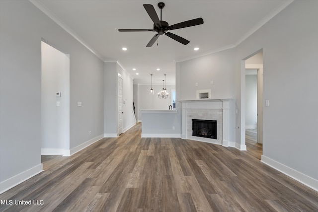 unfurnished living room with ornamental molding, hardwood / wood-style flooring, a tiled fireplace, and ceiling fan with notable chandelier