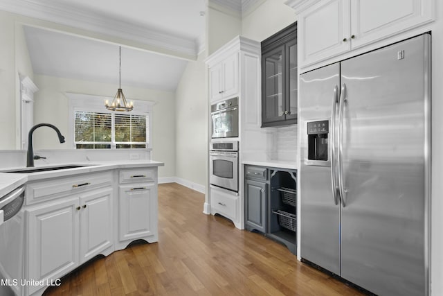 kitchen with a notable chandelier, hardwood / wood-style floors, sink, stainless steel appliances, and white cabinets