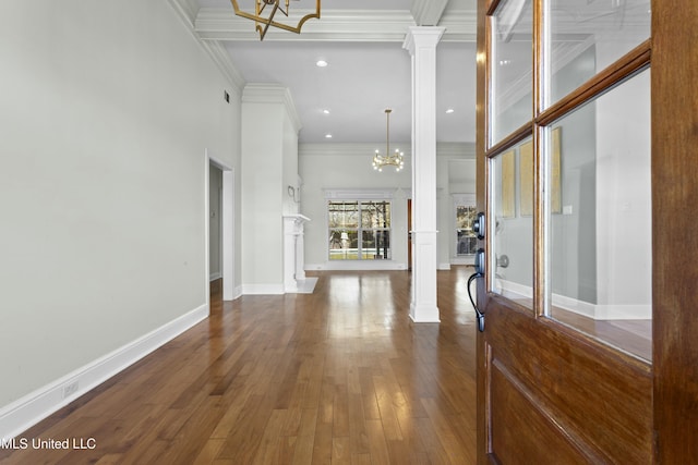 entrance foyer featuring dark wood-type flooring, an inviting chandelier, ornamental molding, and decorative columns