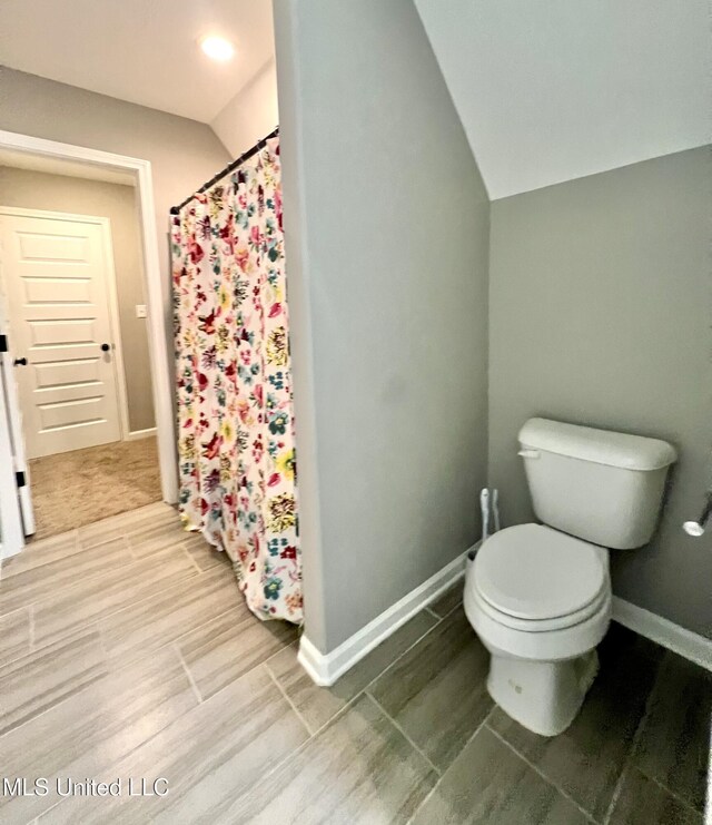 bathroom with hardwood / wood-style flooring, toilet, vaulted ceiling, and a shower with shower curtain