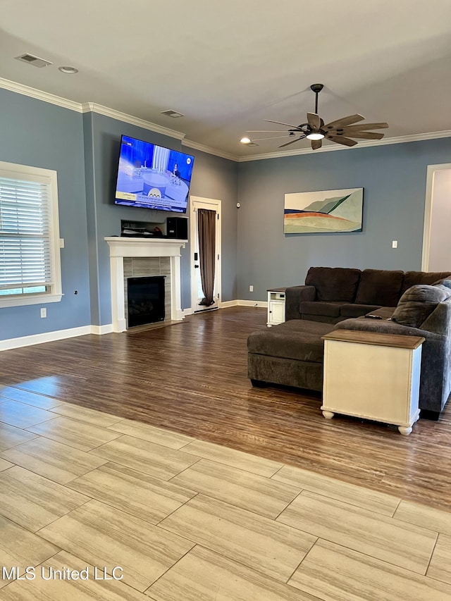 living room with a tile fireplace, crown molding, ceiling fan, and light hardwood / wood-style floors