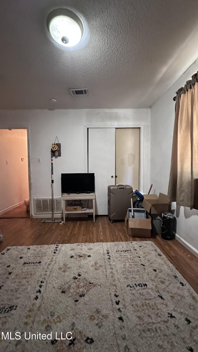 living area with baseboards, a textured ceiling, visible vents, and wood finished floors