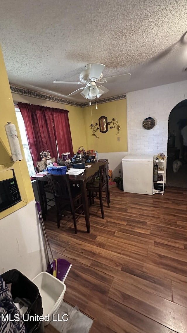 dining room with arched walkways, a textured ceiling, ceiling fan, and wood finished floors