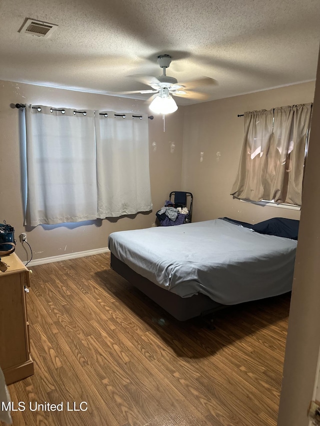 bedroom featuring a textured ceiling, a ceiling fan, wood finished floors, and visible vents